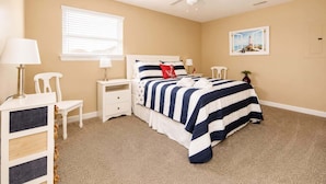A bedroom with a bed, bedside tables, a chair, a lamp, a ceiling fan, a window, and a painting on the wall. - 2BR Beach Bungalow | Walk to Beach | Sleeps 5 (Norfolk)