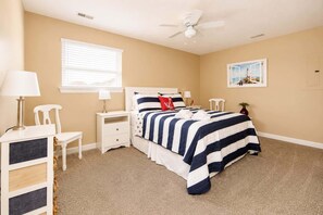 A bedroom with a bed, bedside tables, a chair, a lamp, a ceiling fan, a window, and a painting on the wall. - 2BR Beach Bungalow | Walk to Beach | Sleeps 5 (Norfolk)
