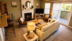 A living room with a fireplace, sofa, TV, and dining area. - Beach Condo 3BR | Deck | Family Friendly (Norfolk)