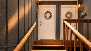 A wooden staircase with a handrail, leading to a door with a wreath. - Beach Condo 3BR | Deck | Family Friendly (Norfolk)