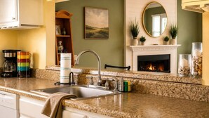 A kitchen with granite countertops, a stainless steel sink, a coffee maker, a colorful mug, a towel, a fireplace, and a mirror. - Beach Condo 3BR | Deck | Family Friendly (Norfolk)
