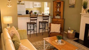 A living room with a sofa, a coffee table, a fireplace, and a kitchen in the background. - Beach Condo 3BR | Deck | Family Friendly (Norfolk)