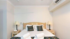 Una habitación de hotel con una cama, dos mesitas de noche, lámparas y un ventilador de techo.