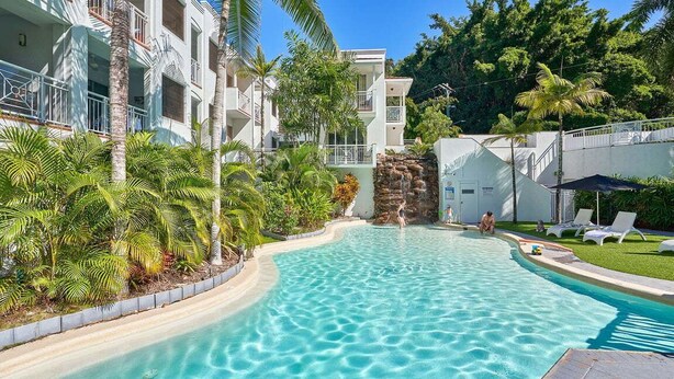 Una piscina rodeada de palmeras y un edificio con balcones.
