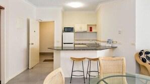 Una cocina compacta con una isla central, dos taburetes de bar y una mesa de cristal.