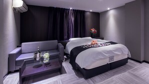 Quarto de hotel moderno com cama, sofá, mesa de centro de vidro e ar condicionado fixado na parede.