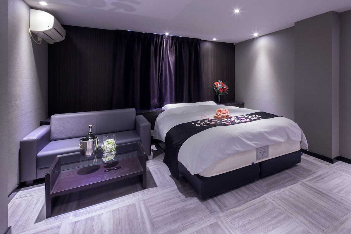 Una habitación de hotel moderna con cama, sofá, mesa de centro de vidrio y aire acondicionado instalado en la pared.