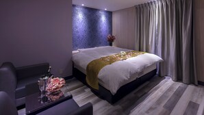 Quarto de hotel com uma cama, um sofá, uma mesinha com um vaso de flores e uma parede com padrão azul.