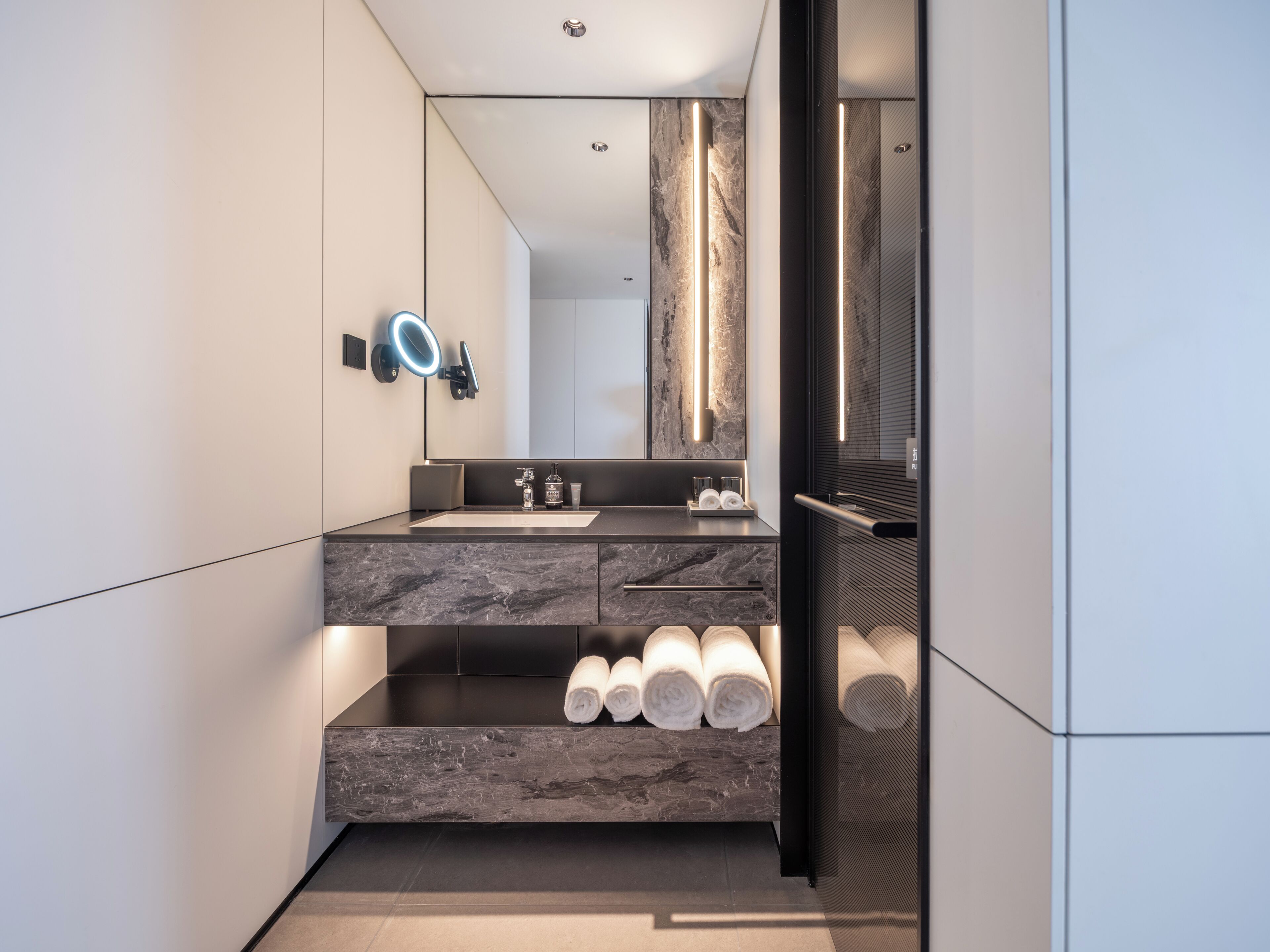 Un baño moderno con un lavabo de mármol, un espejo grande y un perchero para toallas.