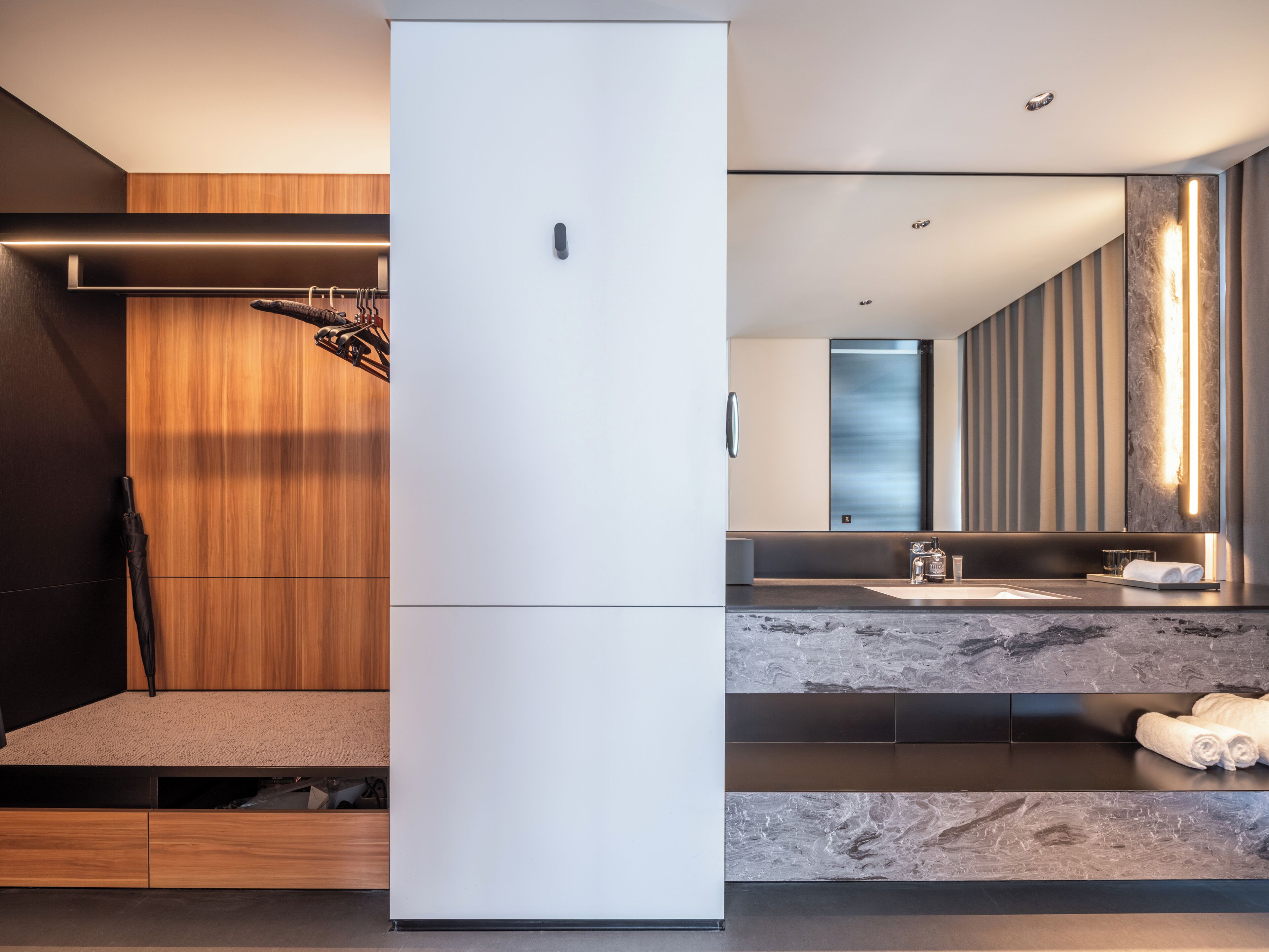 Ein modernes Badezimmer mit großem Spiegel, einem weißen Kühlschrank, Holzschränken und einer Marmorarbeitsplatte.