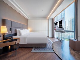 A modern hotel room with a large bed, a TV, a desk, and a view of the city.