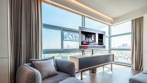 A modern living room with a large TV, grey sofas, and a city view through large windows. - IntercityHotel Dongguan Dongcheng Wanda (Dongguan)
