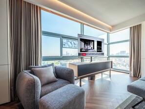 A modern living room with a large TV, grey sofas, and a city view through large windows. - IntercityHotel Dongguan Dongcheng Wanda (Dongguan)