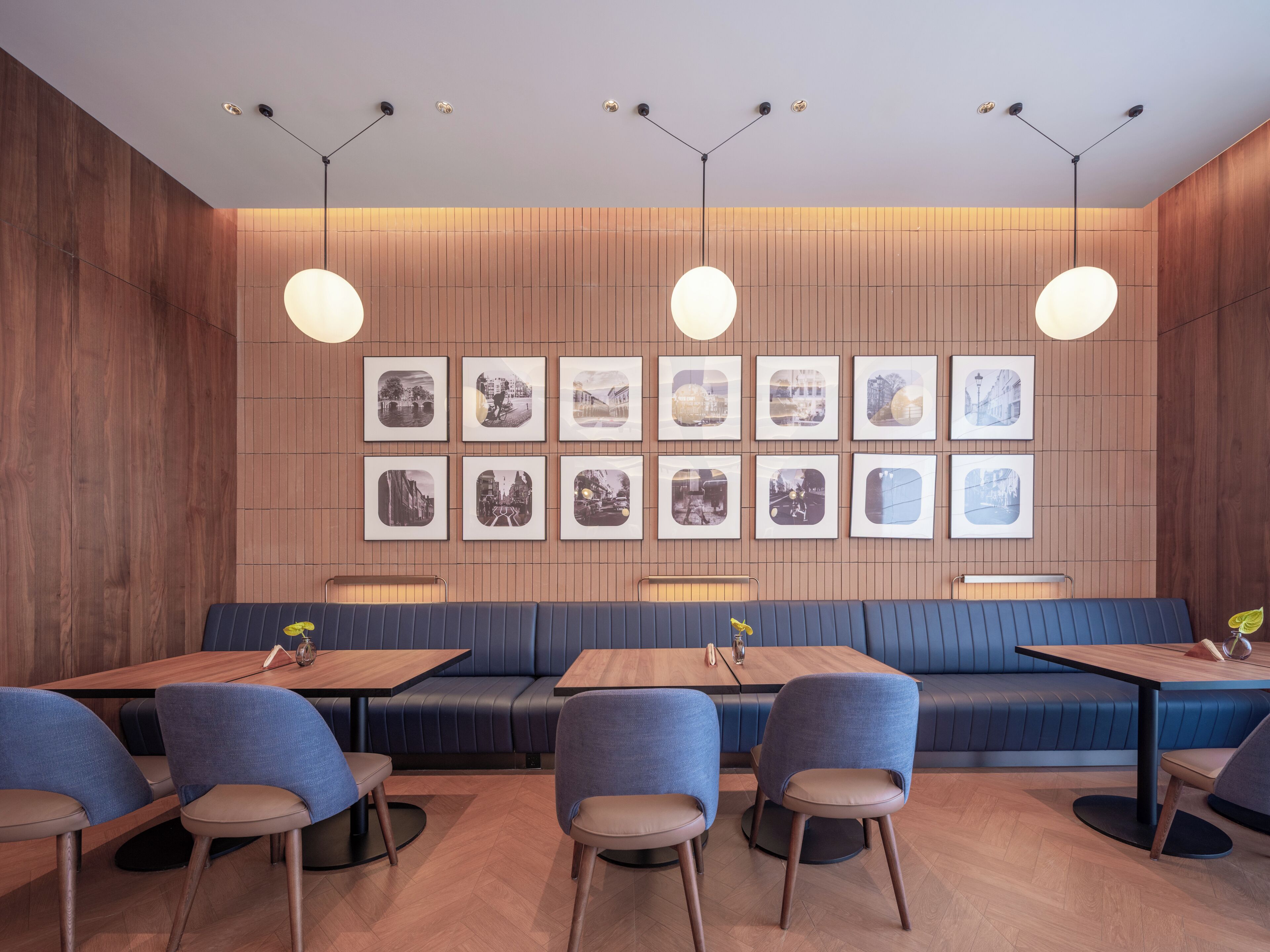 Interior de restaurante con paneles de madera, un largo banco azul y varias mesas con sillas.