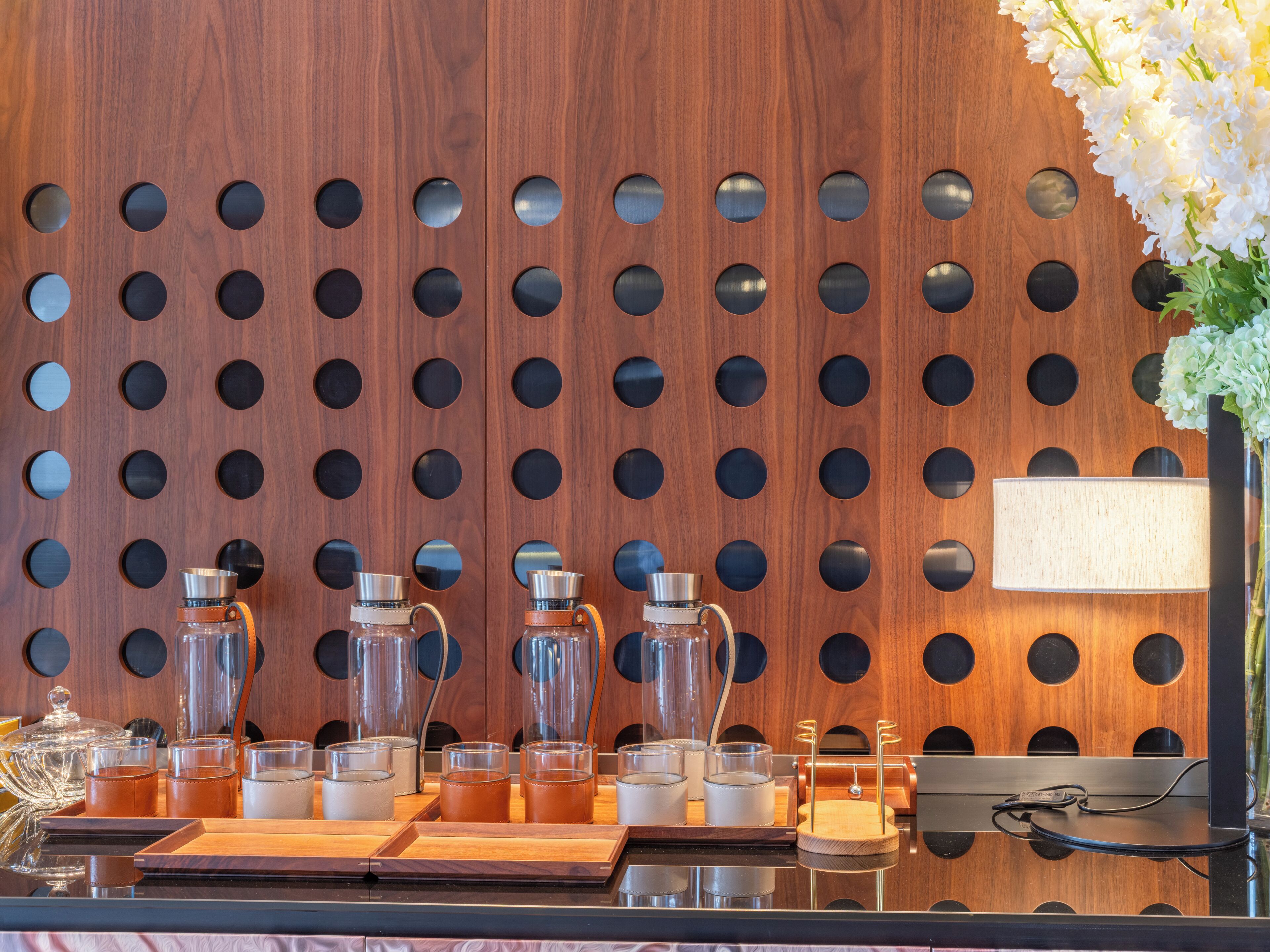 Un mostrador de recepción con un panel de pared de madera, un jarrón con flores y distintos vasos y recipientes.