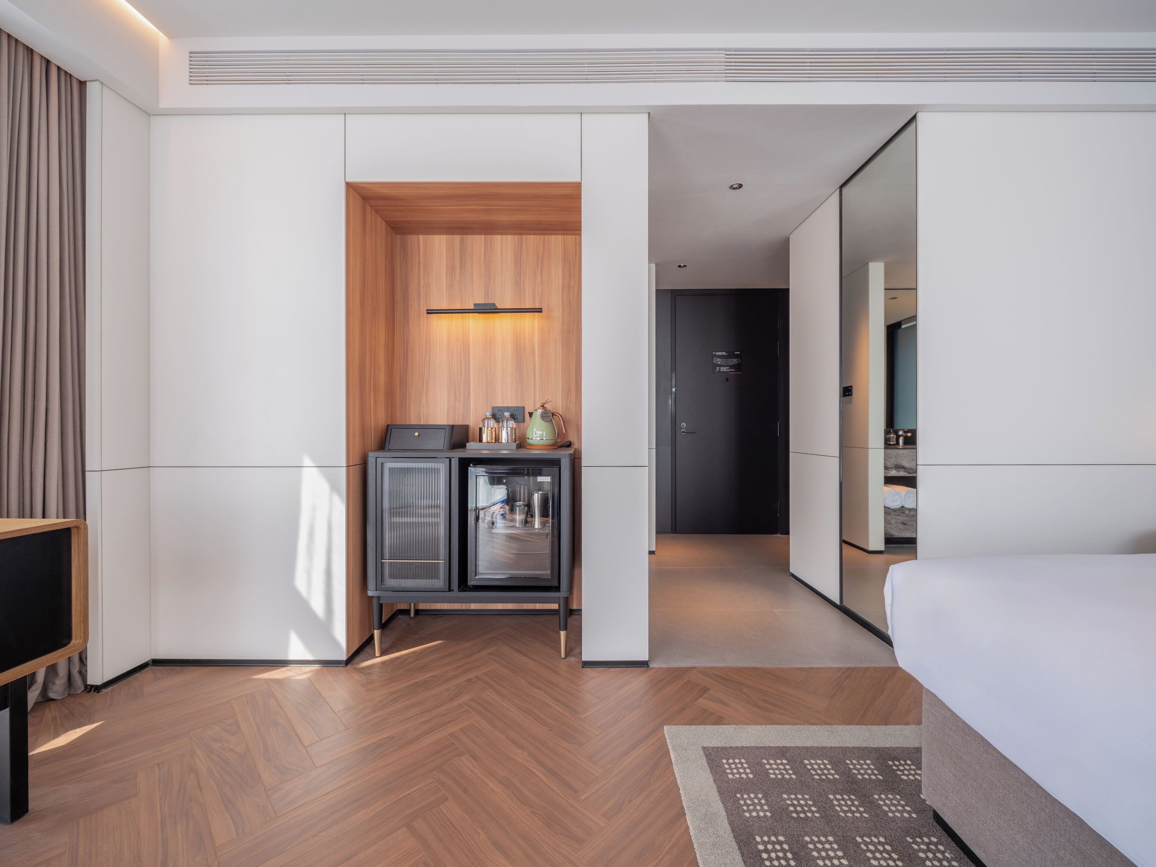 Habitación de hotel con una cama, un pequeño kitchenette, un espejo y una puerta que da a otra habitación.