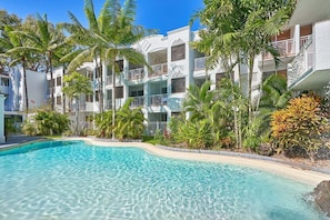 A resort with a swimming pool, palm trees, and multi-story buildings. - Alassio Studio 203-2 (Palm Cove)