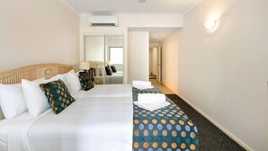 Hotellihuone, jossa on sänky, toinen sänky, kattotuuletin, ilmastointilaite ja valaisin.