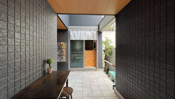 A narrow courtyard with a wooden table and chairs, a potted plant, and a sliding glass door leading to a room with a tiled floor. - 5963 Hotel Higashi Ikebukuro (Tokyo)