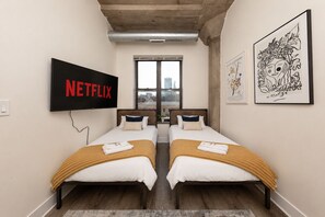 Ett rum med två sängar, en tv som visar ”NETFLIX” och konstverk på väggarna.