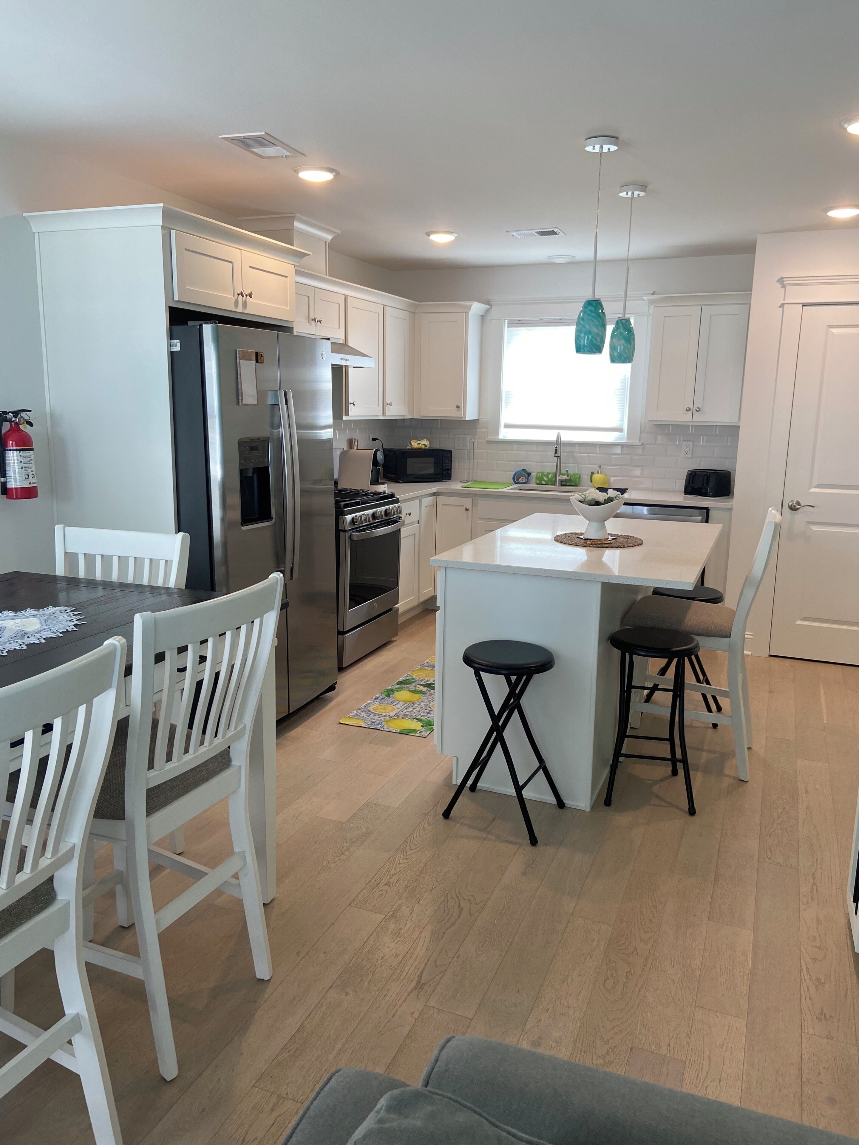 A modern kitchen with white cabinetry, stainless steel appliances, a central island with stools, and a window providing natural light.