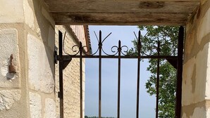 A metal gate with vertical bars and decorative elements, leading to a building with a stone exterior.