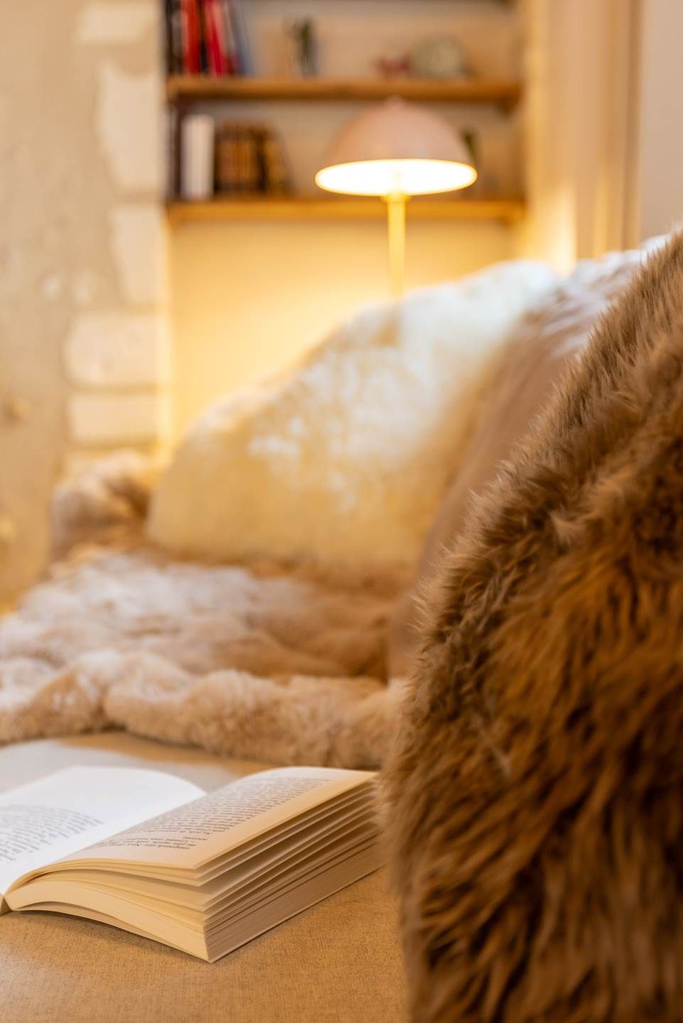 Et hyggeligt rum med en stol betrukket med pels, et blødt tæppe og en lampe på et natbord.