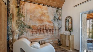 A room with a mural, a white sofa, a stone bench, and a mirror.