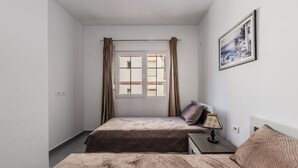 Een slaapkamer met twee bedden, een raam met gordijnen, een nachtkastje met een lamp en een lijst met een afbeelding aan de muur.