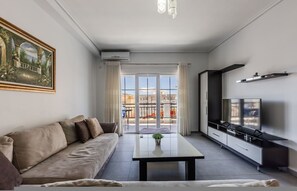 A modern living room with a sofa, a coffee table, a TV, and a balcony with a view. - Flower Balcony Apartment 2BR Beachside Escape (Sarandë)