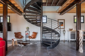 Un interior moderno con una escalera espiral, sillas de cuero, un sofá rojo y una alfombra rústica.