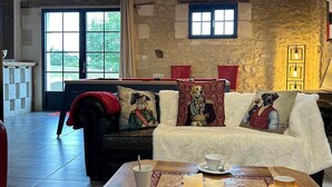 A cozy living room with a stone wall, a wooden ceiling, and a large window. - La Grange - Pleasure in Nature & Calm (FLERE LA RIVIERE)