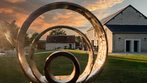 A metal sculpture in the foreground with a building in the background. - La Grange - Pleasure in Nature & Calm (FLERE LA RIVIERE)