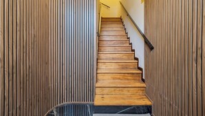 Eine Holztreppe mit Handlauf, gesäumt von vertikalen Holzwänden, die zu einer Zwischenebene mit einem an der Wand befestigten Schild führt.