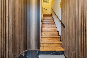 A wooden staircase with a handrail, flanked by vertical wooden panels, leading to a landing with a wall-mounted sign. - Garrett Elegance (Setúbal)