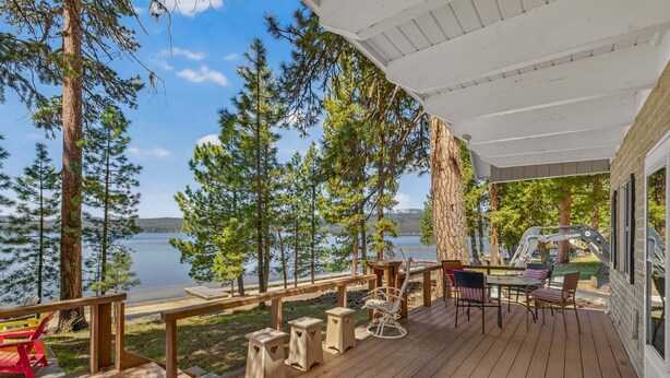 Terraza de madera con mobiliario exterior con vista a un lago, rodeada de árboles.