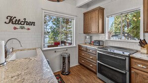 Una cocina con lavamanos, estufa, armarios y ventana con vistas a árboles.