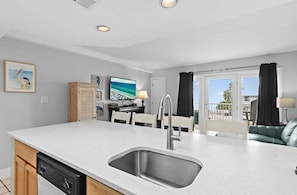 A modern kitchen with a large island, a built-in dishwasher, and a dining area with a table and chairs. - Beach Service Included! Gulf View! Private Beach! Gulfview I 213! (Miramar Beach)