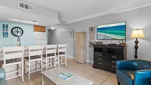 Uma sala de estar com uma mesa de jantar, cadeiras, uma televisão, um abajur e um armário.