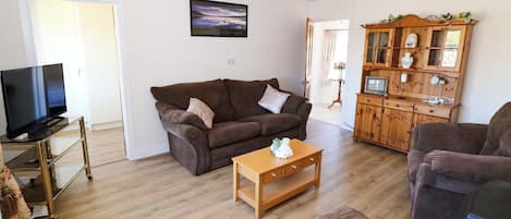 A living room with a sofa, a coffee table, a television on a stand, and a wooden cabinet with glass doors.