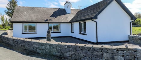A white house with a stone wall foundation, a sloped roof, and a stone pillar in front.