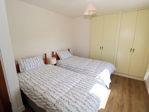 A bedroom with two beds, a wardrobe, and a ceiling lamp. - CAHIR COTTAGE, family friendly in Ballinrobe, County Mayo (Ballinrobe)