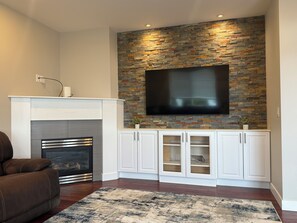 Ein Wohnzimmer mit Kamin, einem an der Wand befestigten Fernseher, weißen Schränken und einem gemusterten Teppich.
