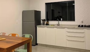 A kitchen with a refrigerator, a window, a countertop, and a dining table with chairs. - Charming retreat with fireplace and nature views in Pomerode. (Pomerode)