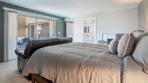 Un dormitorio con una cama grande, una puerta corrediza de vidrio que da a un balcón, una mesita y un espejo.