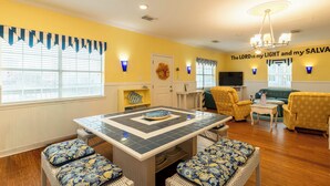 A dining area with a table and chairs, a sofa, a television, and a wall with a religious quote. - Ocean View l Big 5BR Home l Easy Beach Access (Surfside Beach)
