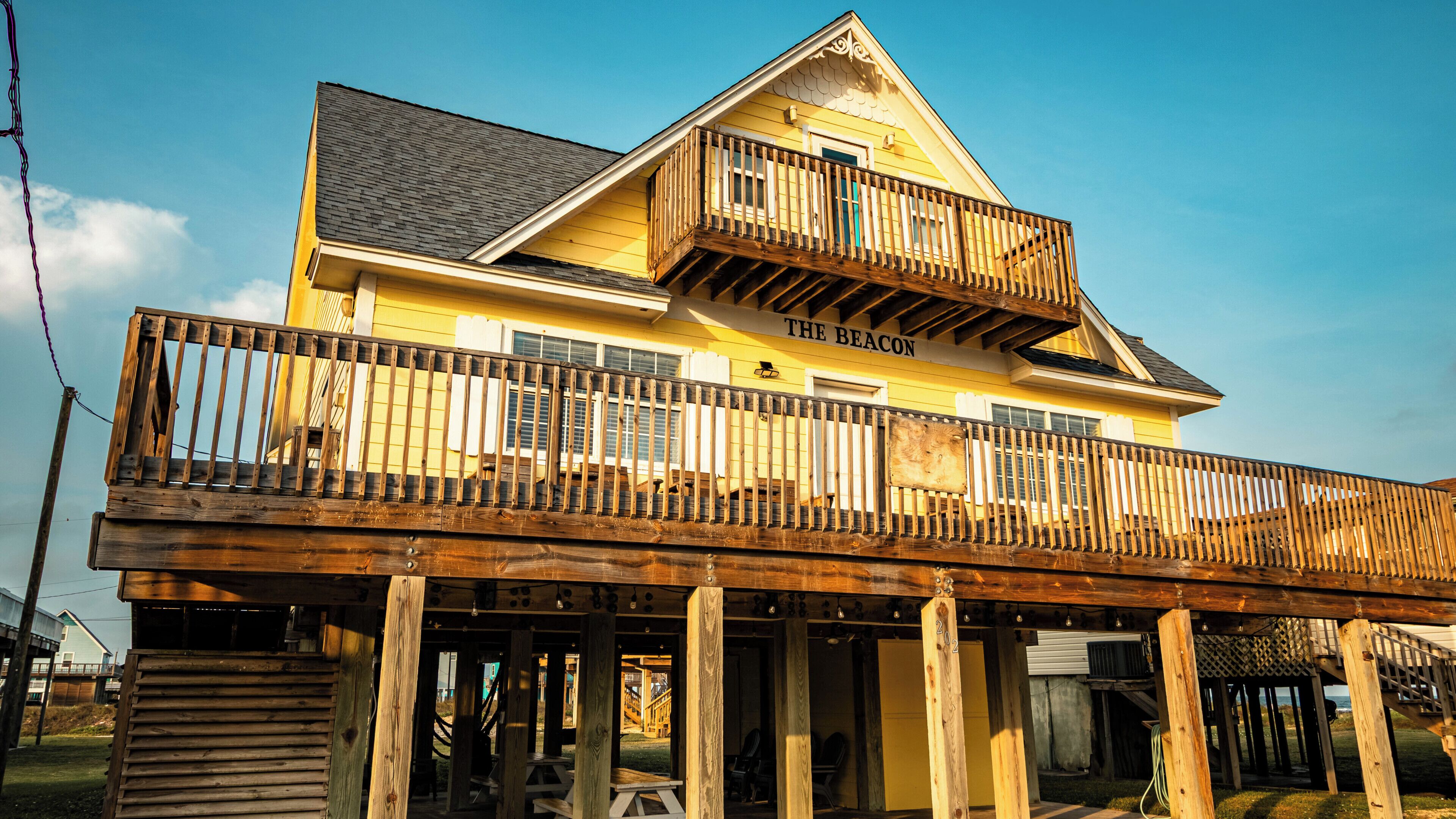 A two-story building with a balcony, labeled 'The Beacon,' featuring a wooden deck and a view of the surrounding area.