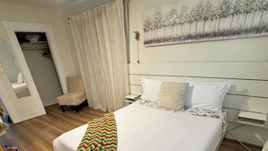 Un letto rifatto con cura, una coperta decorata, una testata con un quadro e un pavimento in legno.