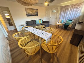 Ein Essbereich mit einem Glastisch, Holzstühlen, einem grauen Sofa und einem Deckenventilator.