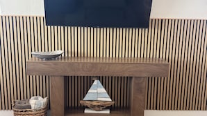 Un tavolo in legno con una TV a schermo piatto montata sopra, un cesto di vimini con cuscini e un oggetto decorativo in legno sul tavolo.